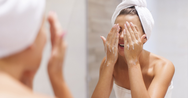 Woman applying  Kajo cleansing gel, surrounded by natural skincare ingredients.